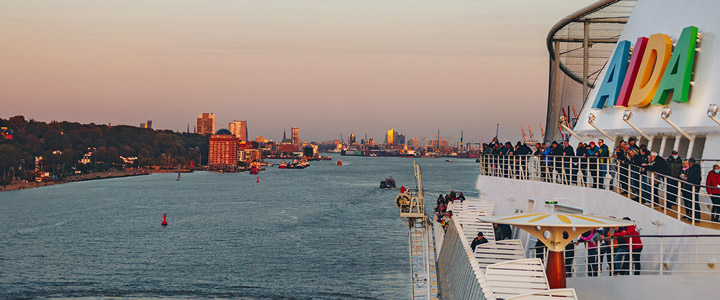 Blick vorbei am AIDA Logo von Bord der AIDAsol auf den Hafen Hamburgs im Hintergrund.